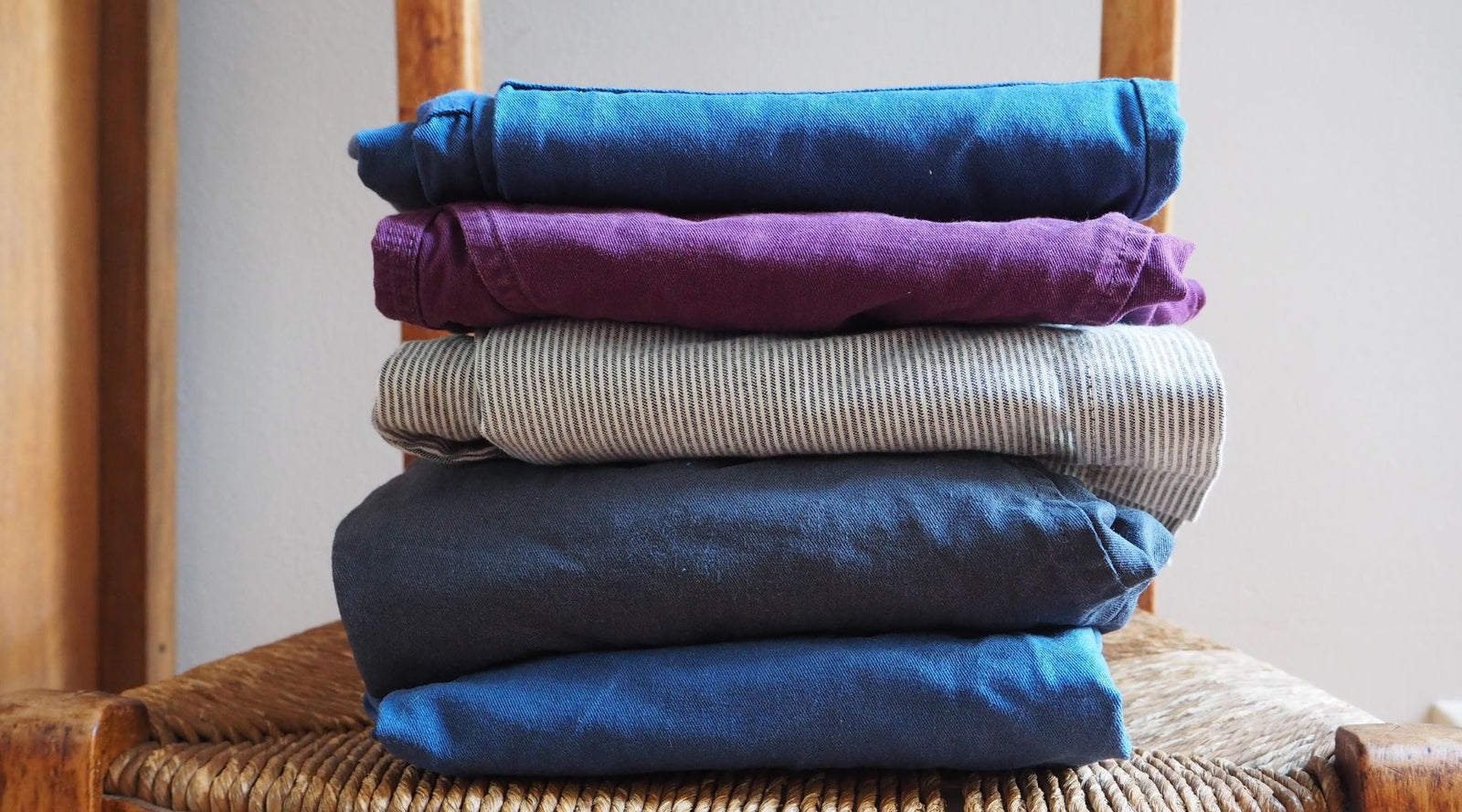 Stack of neatly folded colorful kids clothes on a wooden chair, Jackalo sustainable apparel