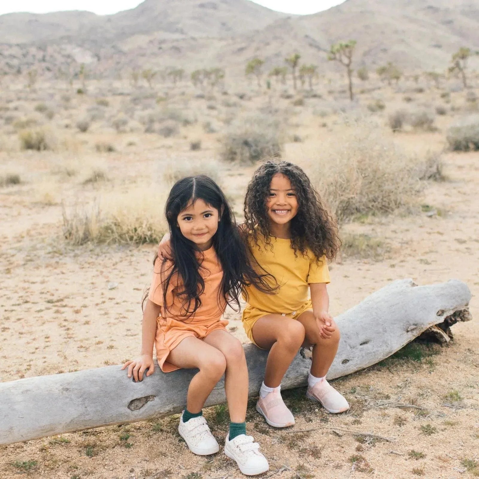 Two girls in Jackalo sustainable kids clothing sitting on a log in a desert landscape