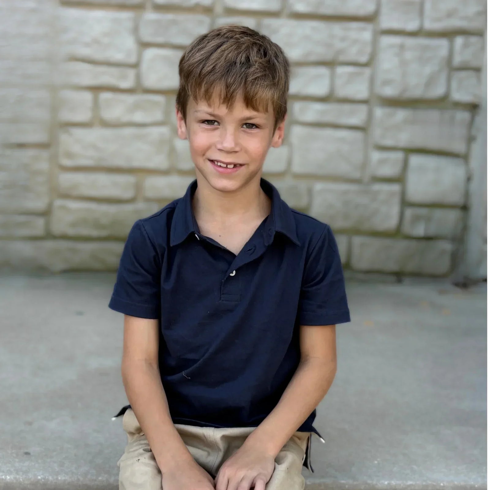 Smiling child wearing a navy polo shirt and khaki pants, sitting outdoors, Jackalo kids clothing