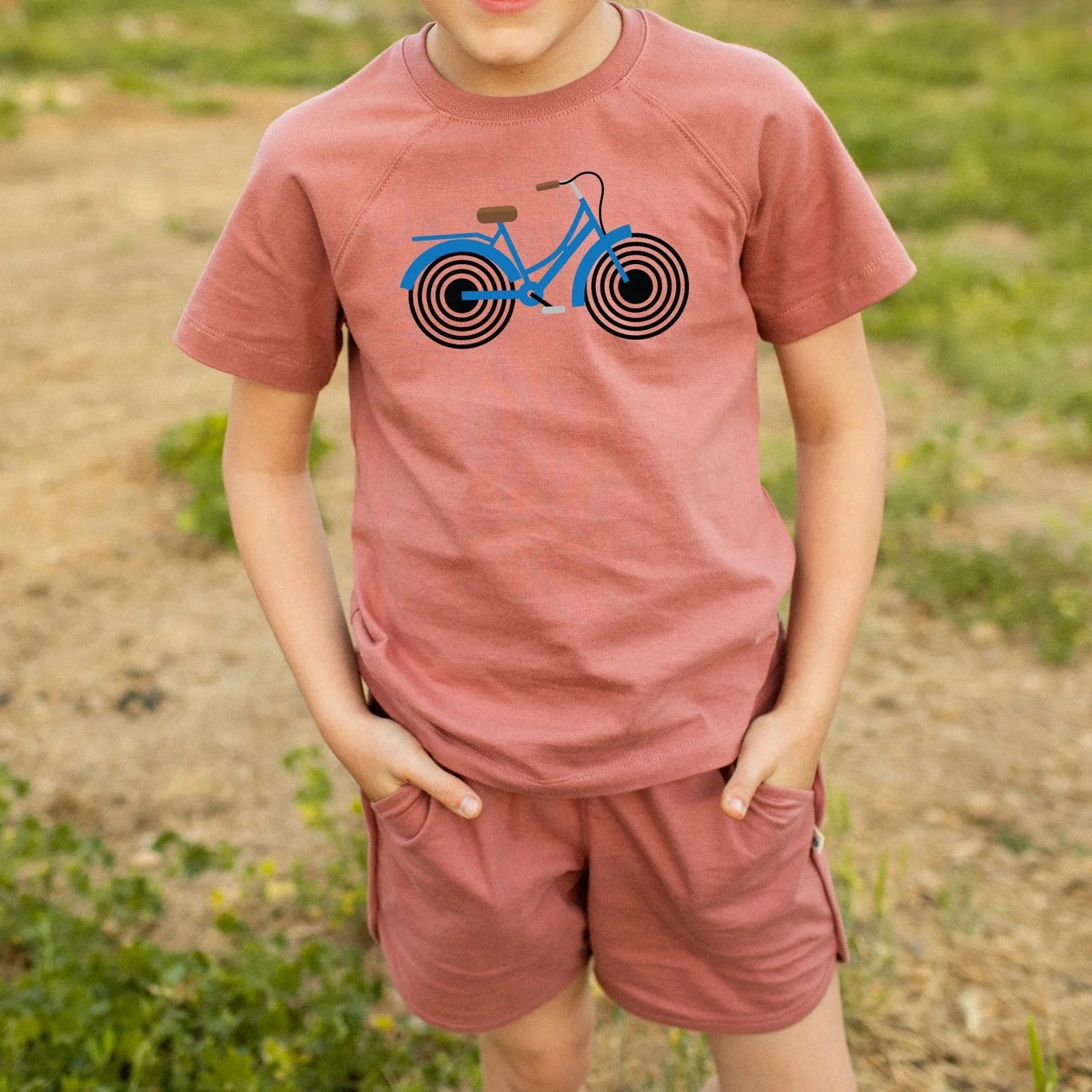 Child wearing a pink t-shirt with a blue bicycle graphic outdoors.