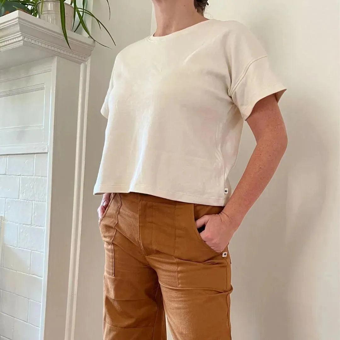 Adult wearing Jackalo sustainable cream t-shirt and brown pants by a white fireplace.