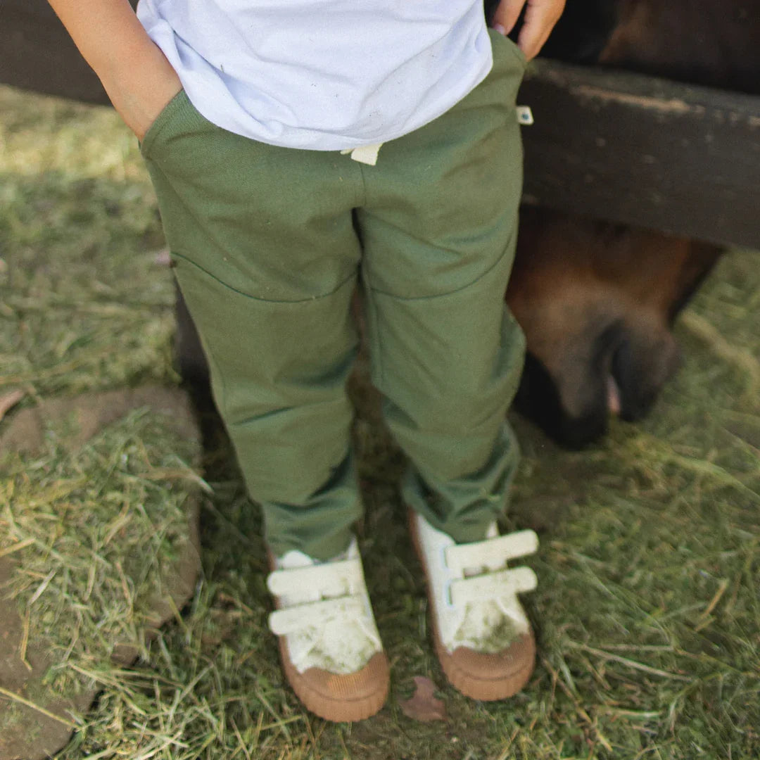 Person wearing green pants and white shoes standing next to a horse on grass.