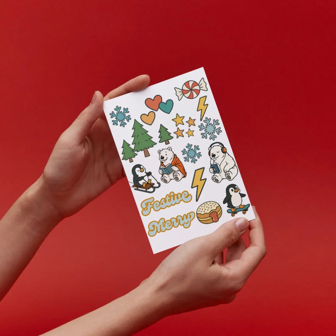 Hands holding festive Jackalo kids sticker sheet with polar bears, penguins, trees, and hearts on red.