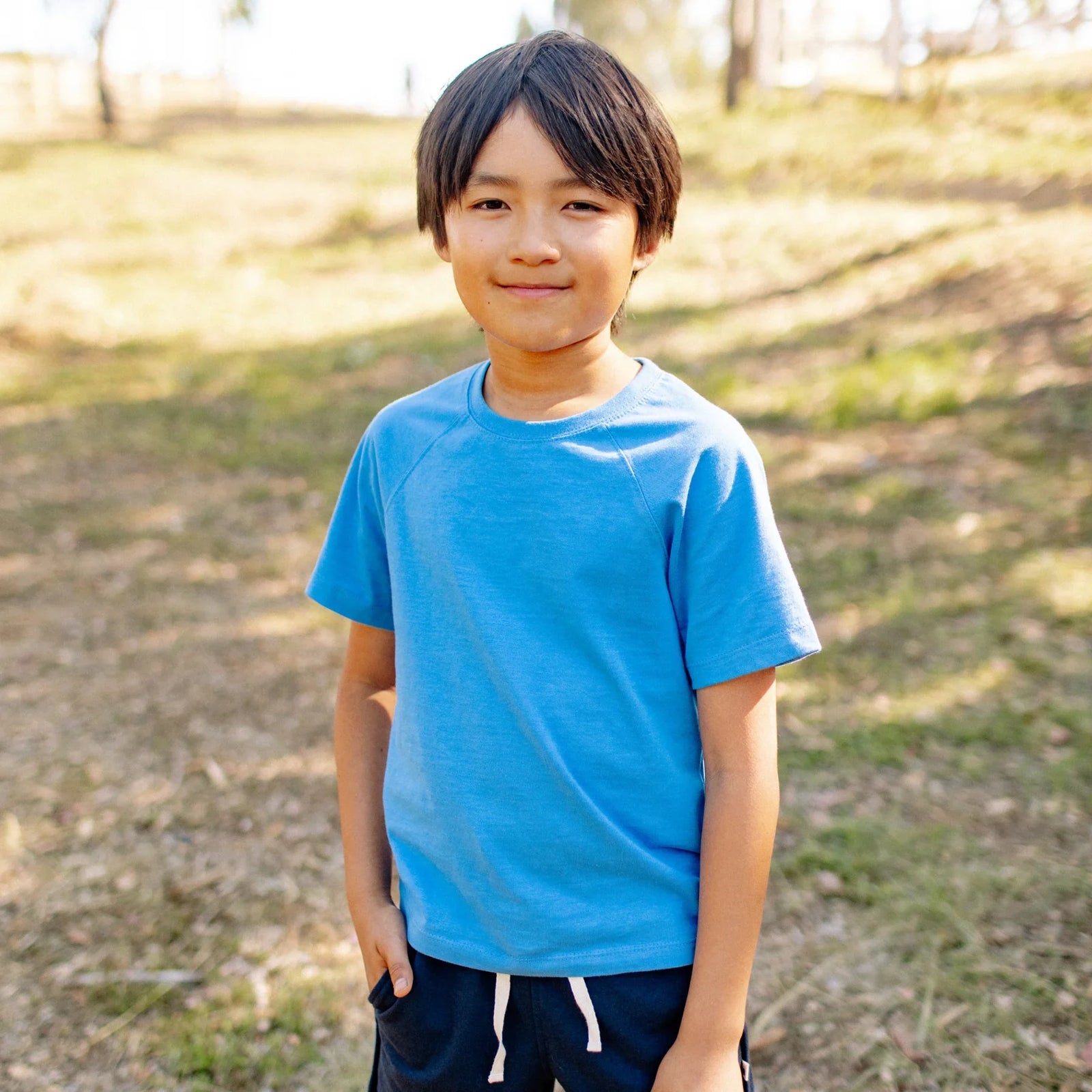 Smiling child outdoors wearing a blue Jackalo sustainable kids t-shirt and navy shorts.