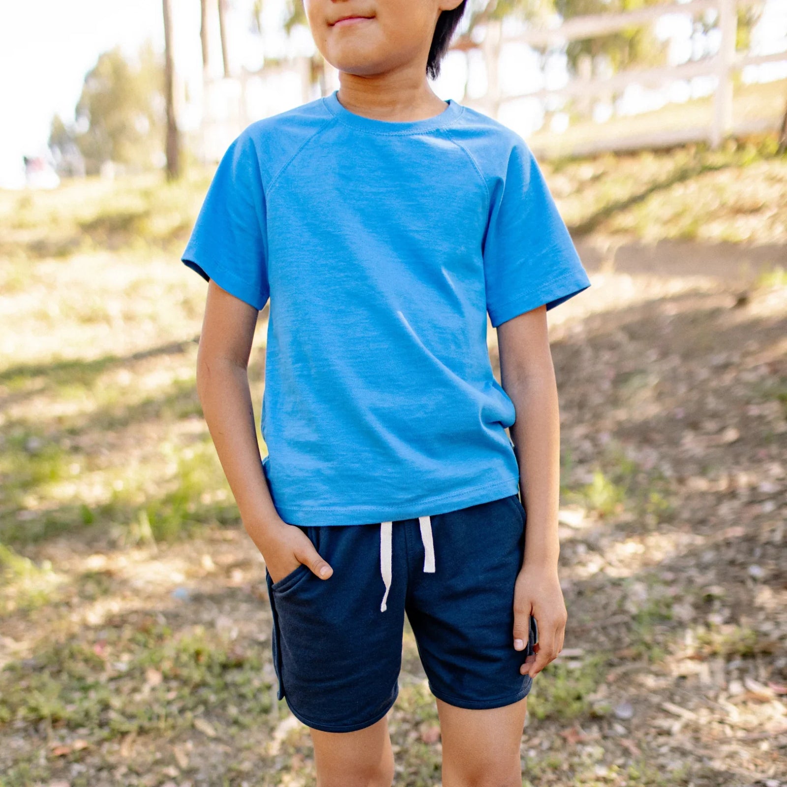 Child wearing Jackalo sustainable blue t-shirt and navy shorts outdoors