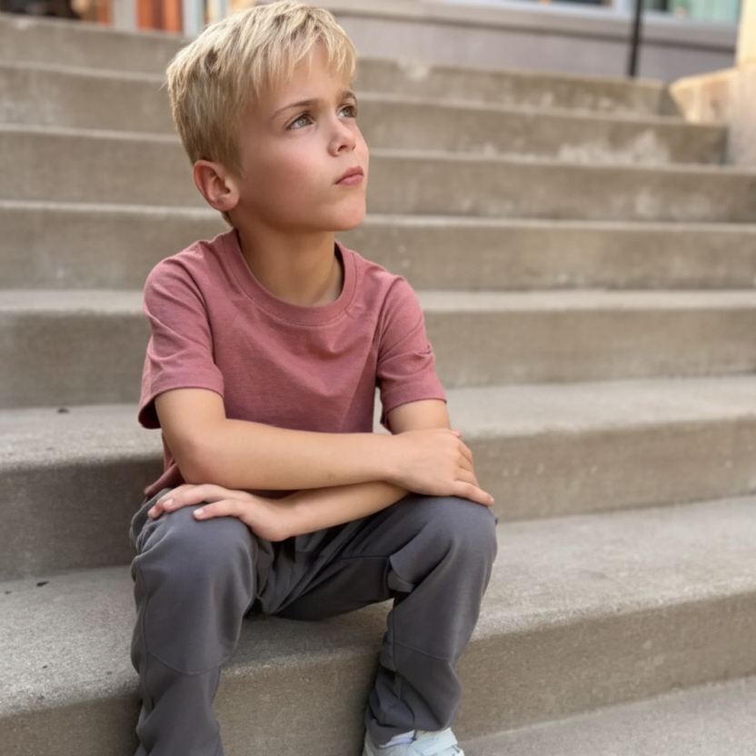 Blonde boy in pink t-shirt and gray pants by Jackalo sitting on outdoor steps