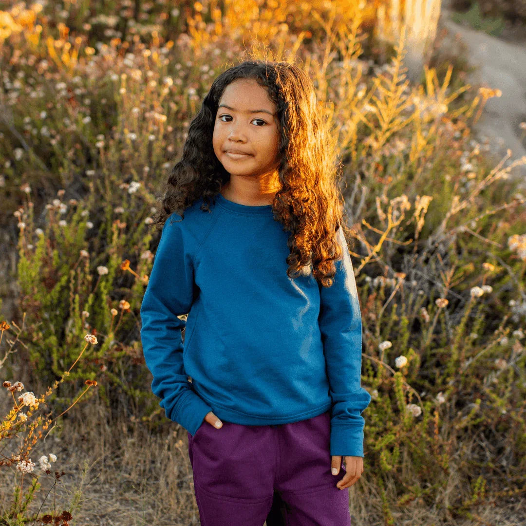 Child wearing Jackalo organic peacock blue sweatshirt outdoors in nature at sunset