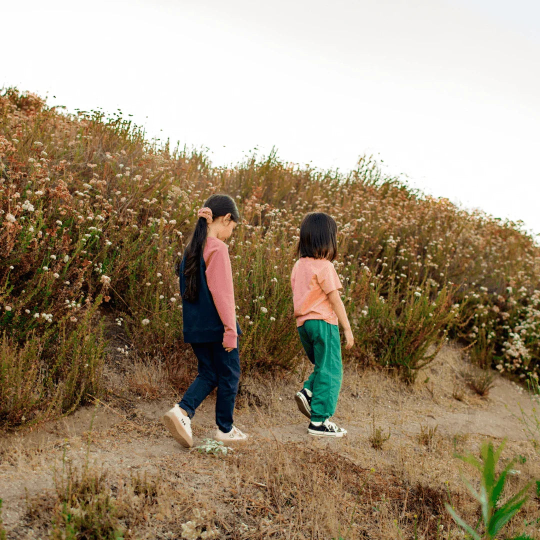 Two kids wearing Jackalo sustainable sweatpants and tees walking outdoors on a dirt path.