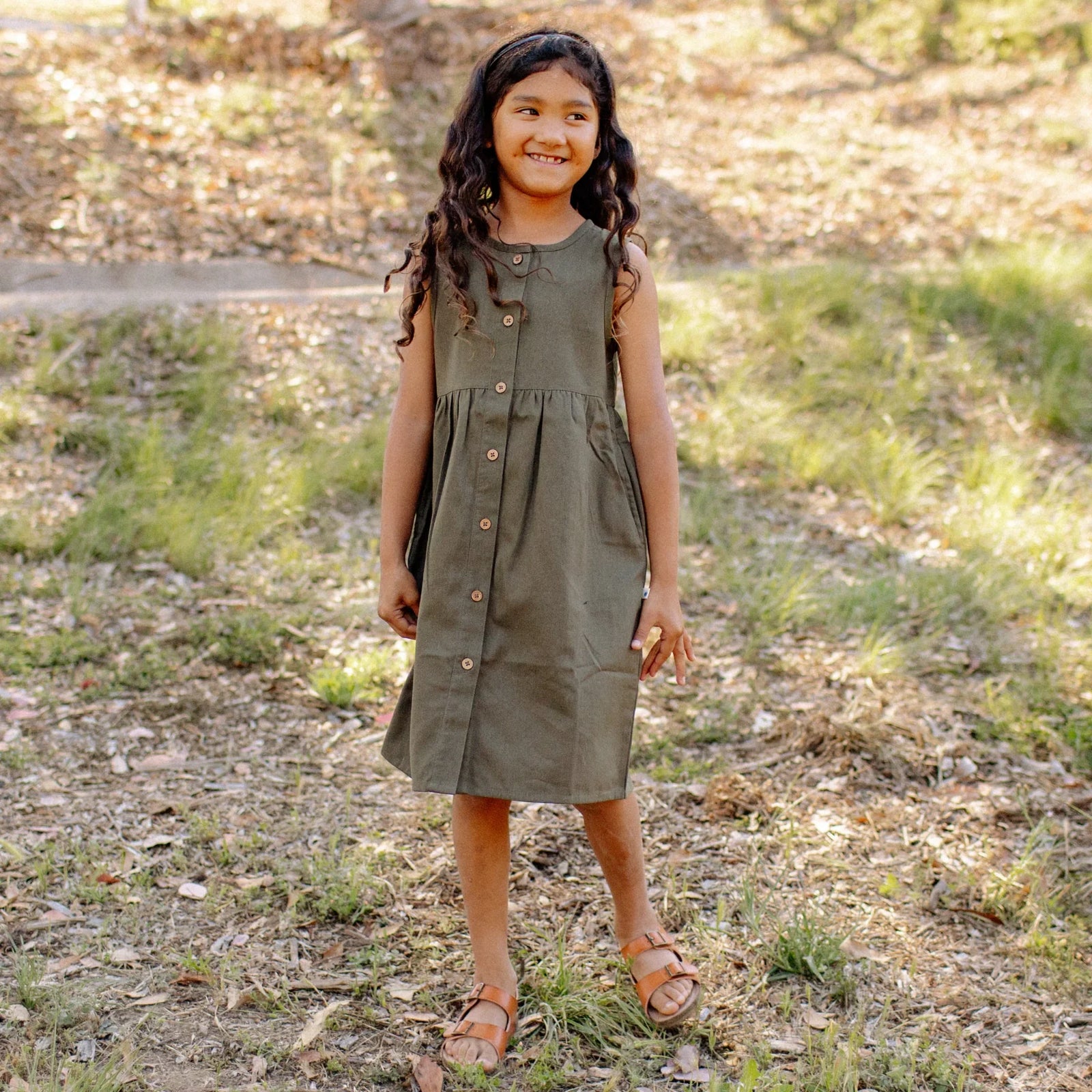 Smiling girl outdoors in olive green sleeveless dress from Jackalo, sustainable kids clothing