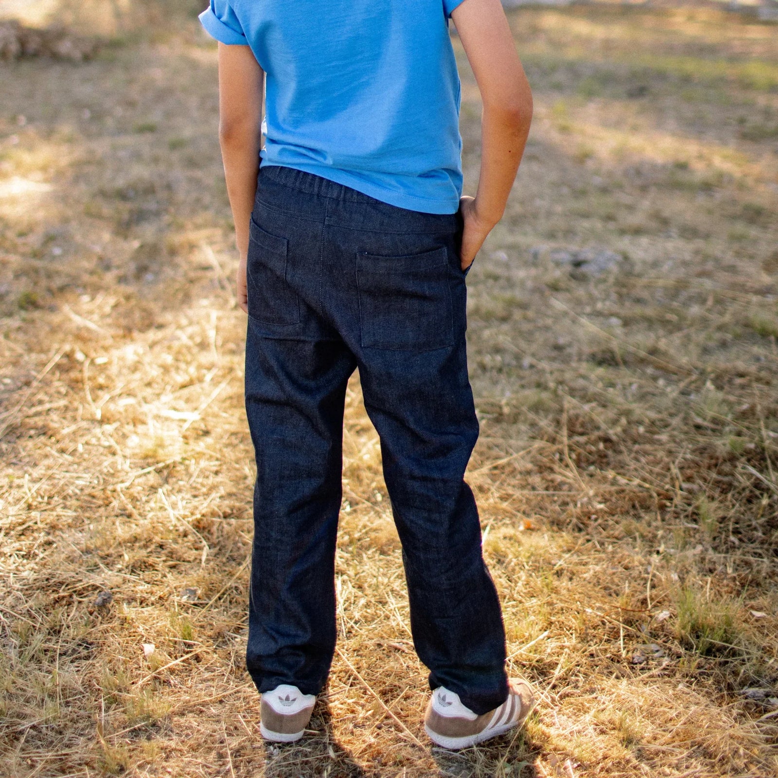 Child wearing dark denim Jackalo jeans outdoors, sustainable kids clothing, back view