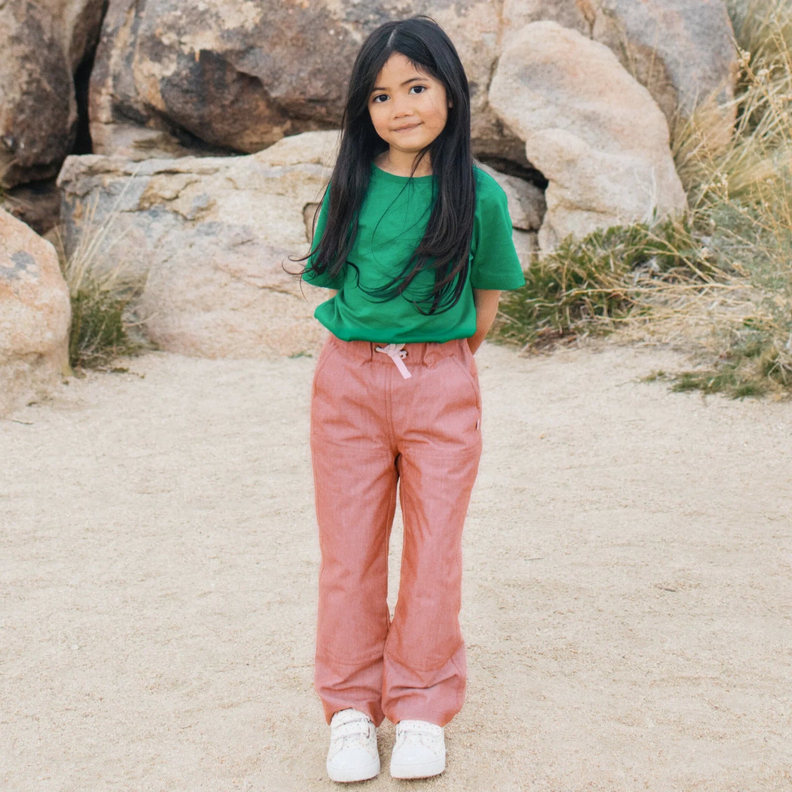 Girl wearing Jackalo Jules chambray pants and green shirt outdoors, sustainable kids fashion