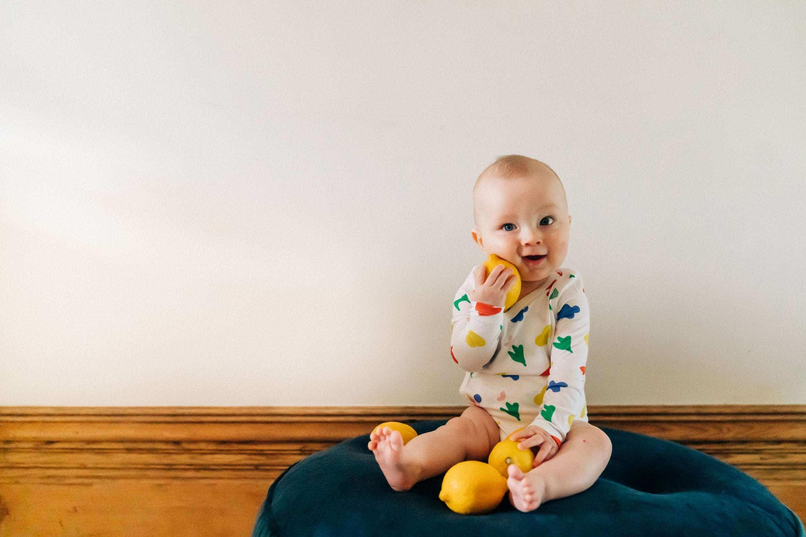 Baby in colorful Jackalo organic onesie sitting on blue cushion with lemons, sustainable kidswear