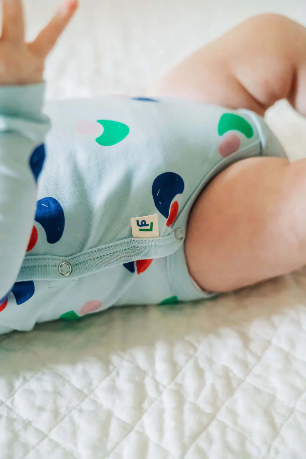 Baby wearing Jackalo sustainable blue bodysuit with colorful print on a white quilt
