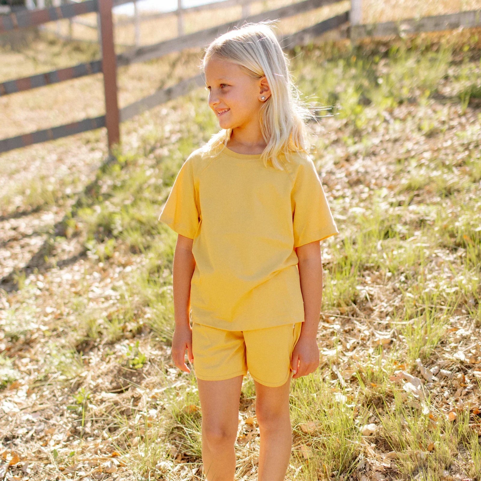 Smiling child wearing yellow Jackalo shorts and t-shirt, standing outdoors in sunlight