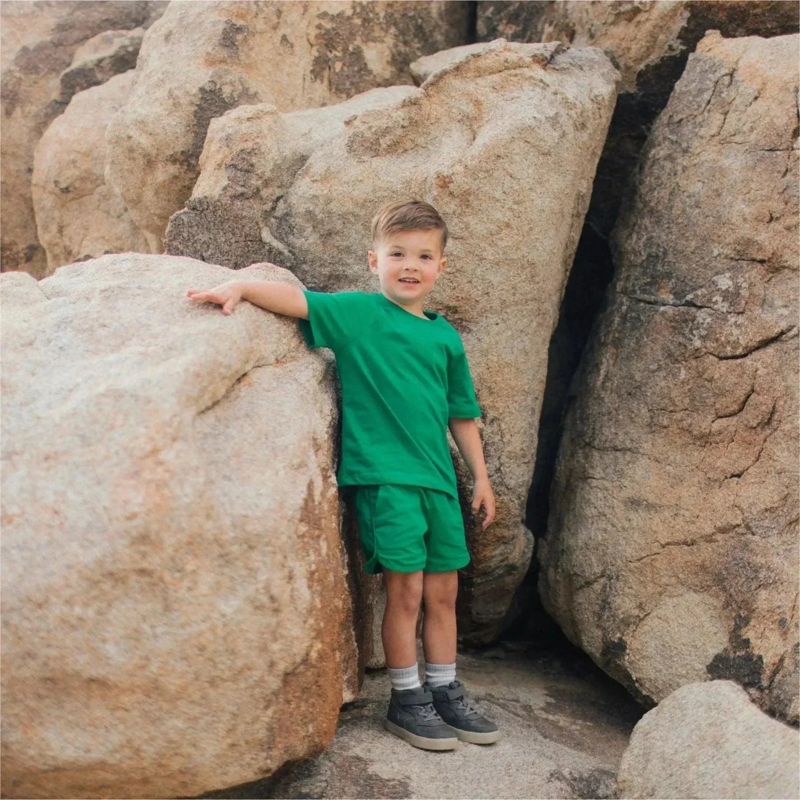 Young boy in green Jackalo shorts and t-shirt standing among large outdoor rocks