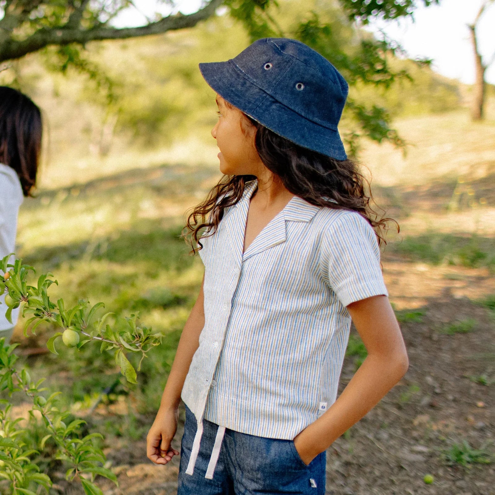 Child wearing reversible denim hat and striped shirt outdoors in sustainable kids clothing by Jackalo