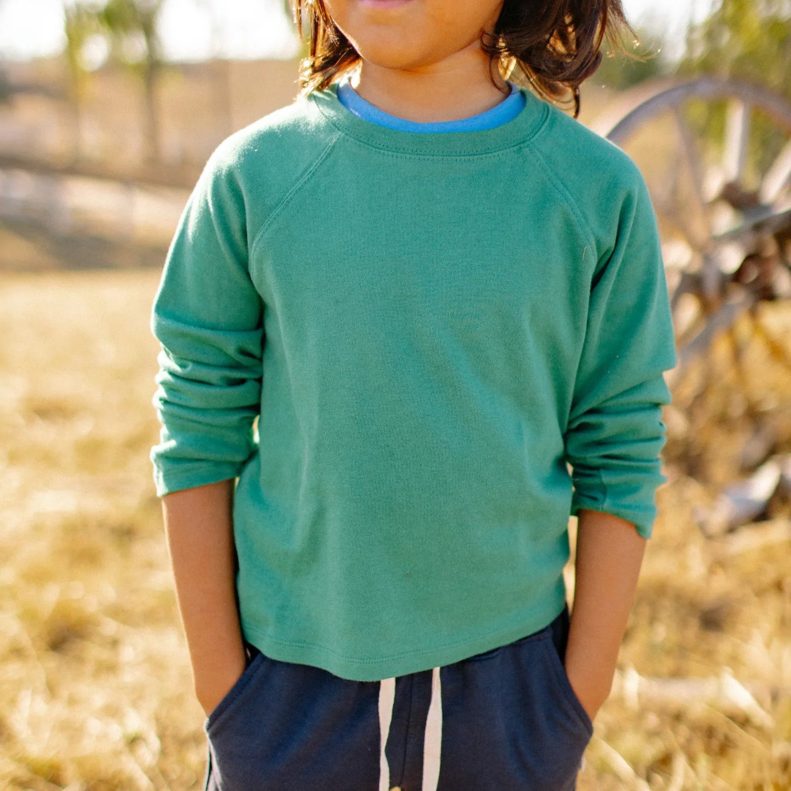 Child wearing green Jackalo sweatshirt and navy pants outdoors in a sunny field