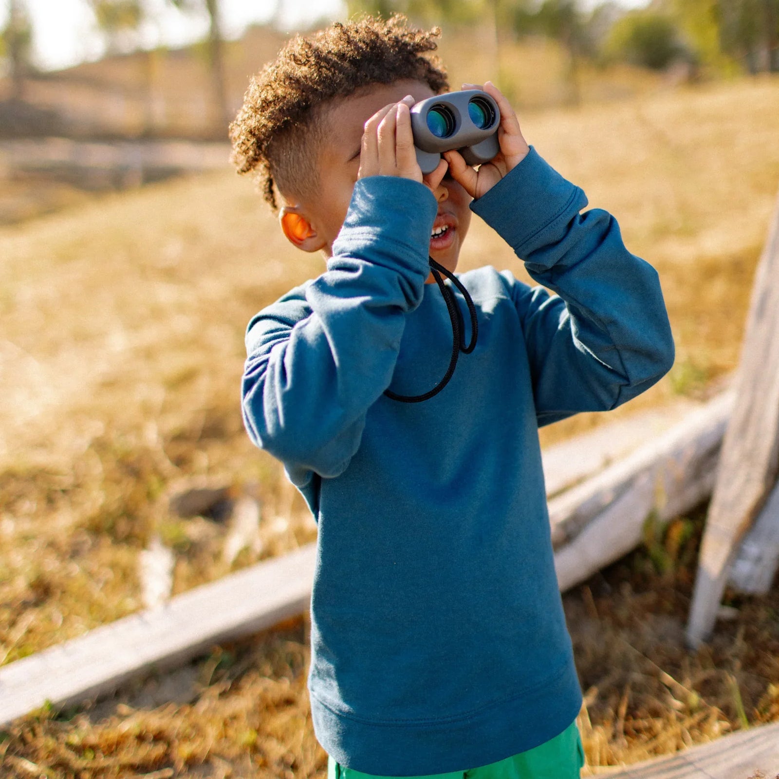 Child in blue Jackalo sweatshirt outdoors using binoculars, active kids sustainable clothing