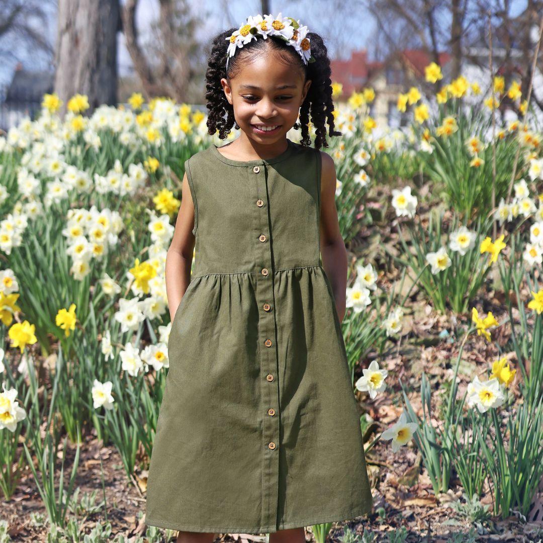 Girl wearing Jackalo dark olive dress and floral headband, standing in a daffodil field