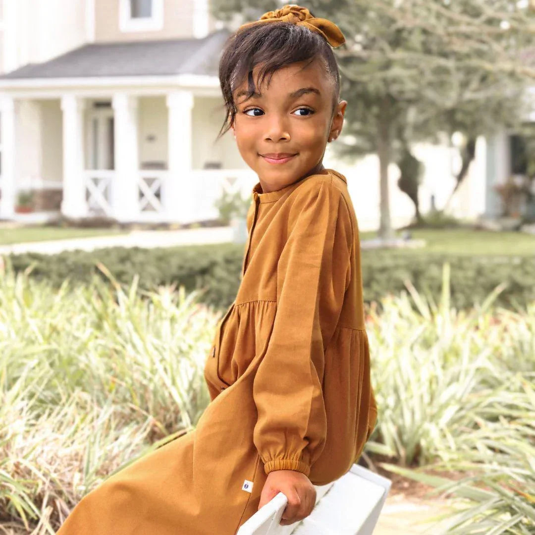 Smiling child in long-sleeved acorn brown Jackalo dress sitting outdoors
