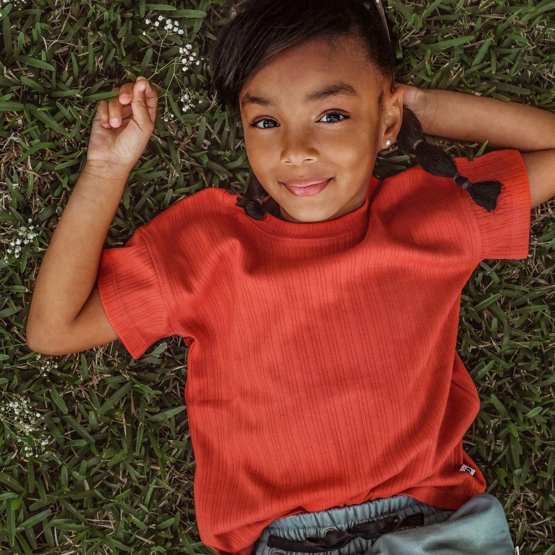 Child in a persimmon ribbed Jackalo t-shirt lying on grass, sustainable kids clothing