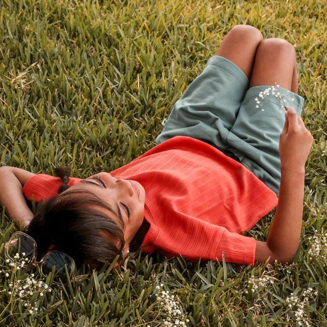 Child in persimmon ribbed Brooklyn t-shirt and green shorts by Jackalo lying on grass