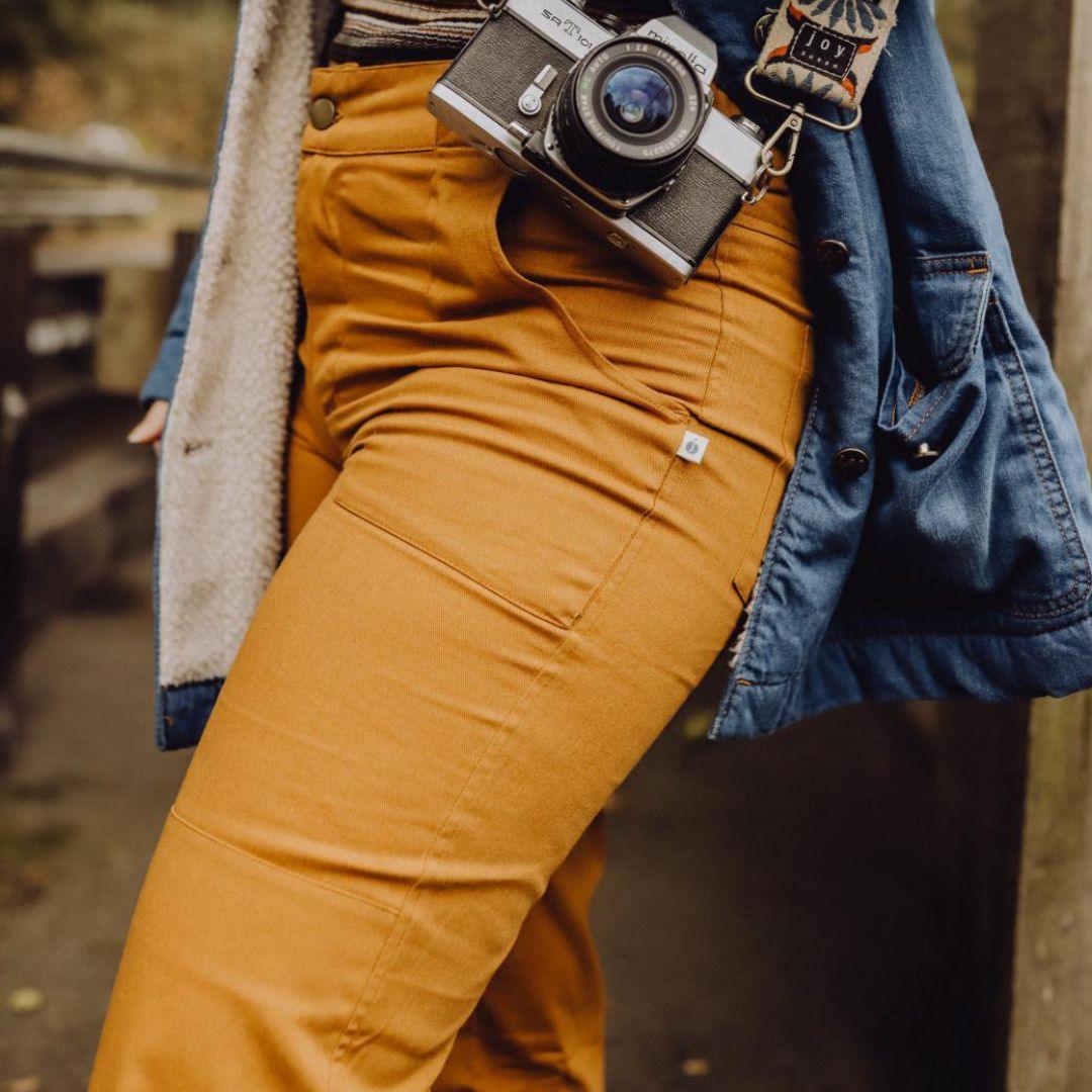 Woman wearing acorn brown Jackalo Charlie pants and blue jacket, holding vintage camera outdoors