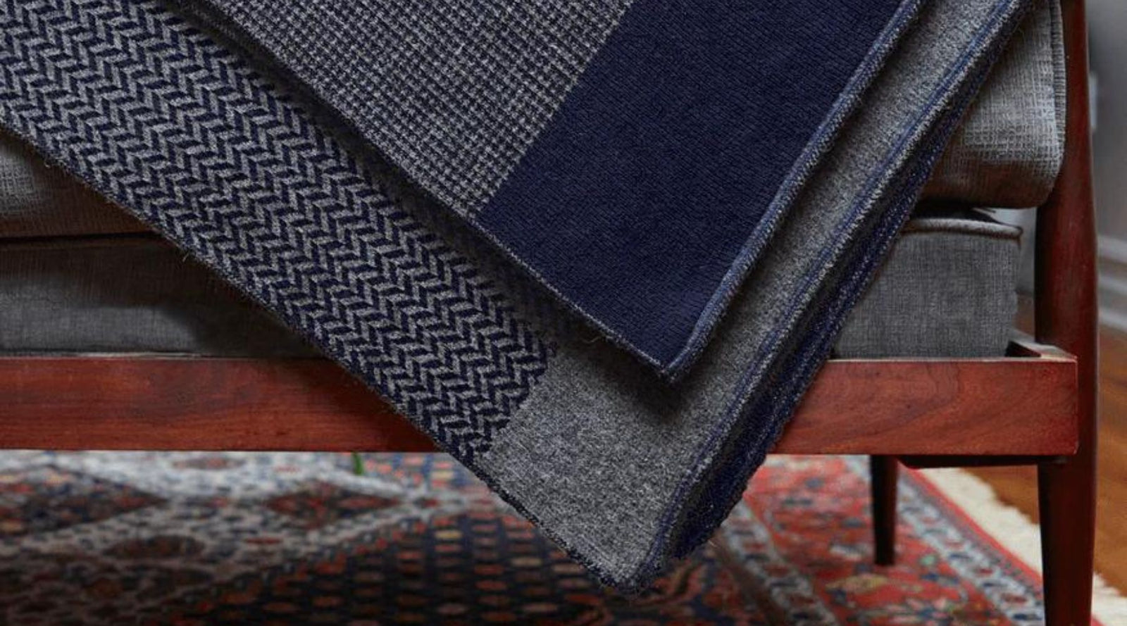 Eco-friendly navy and gray patterned blankets draped over a modern wooden sofa, Jackalo style