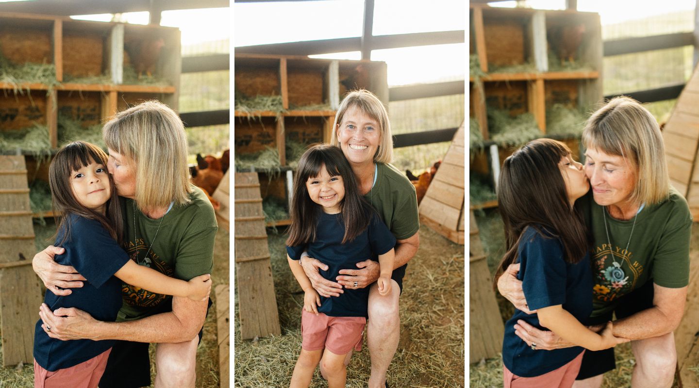 Mom and daughter in cozy kids clothes hugging in a barn with chickens, showcasing comfort and sustainability.
