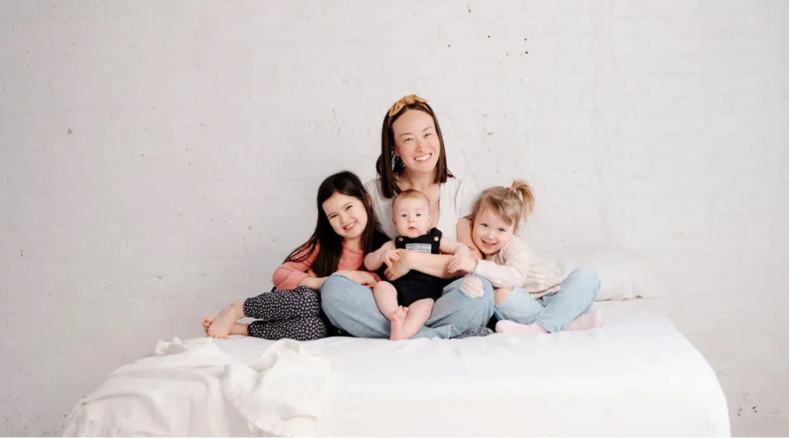 Smiling mom with three kids in sustainable Jackalo kids clothes on a white bed.