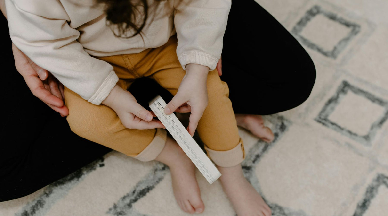 Child in sustainable Jackalo clothing sitting on patterned rug, holding a book