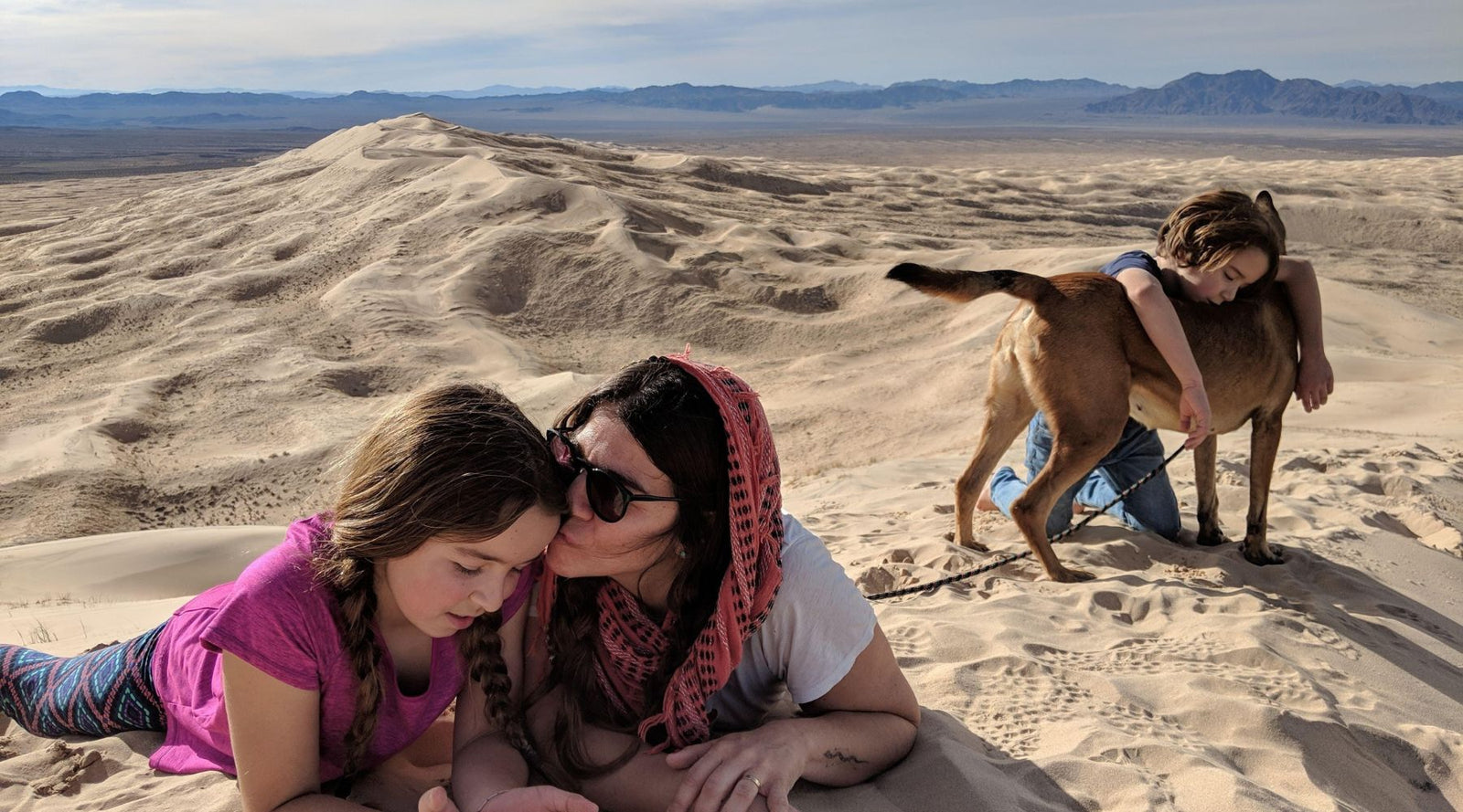 Woman with two kids and a dog relaxing on a sandy hill, wearing Jackalo active kids clothes