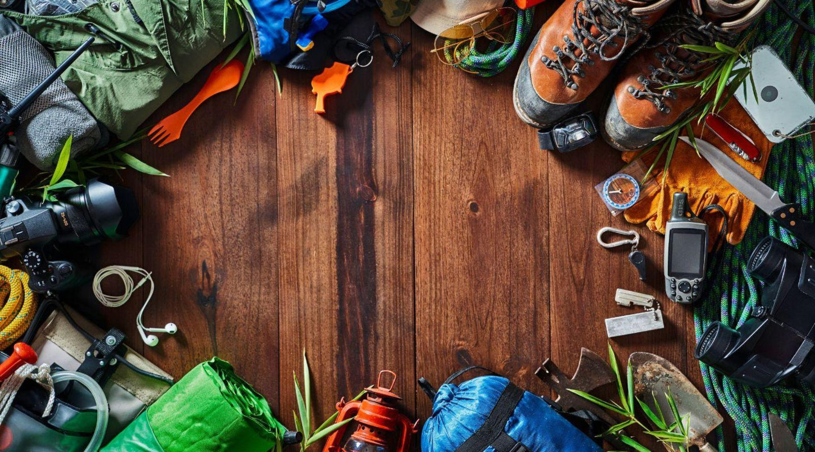 Assorted camping gear on wooden surface, including hiking boots, backpack, rope, camera, and gloves