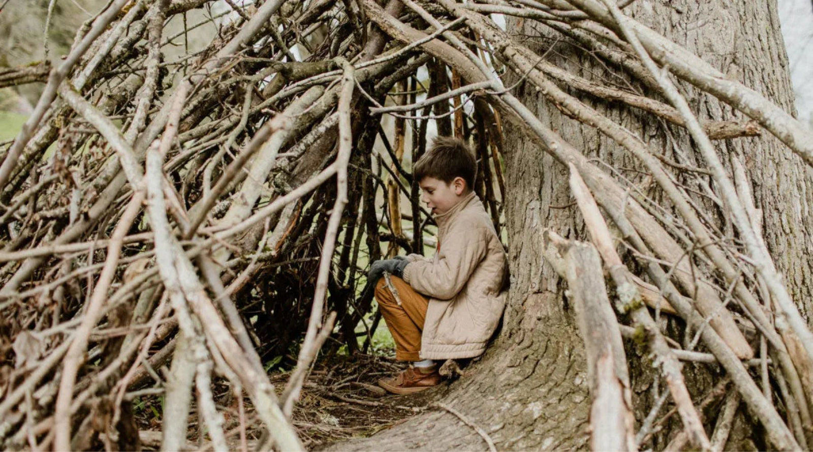 Young boy in Jackalo sustainable kids clothes under a tree branch tent outdoors