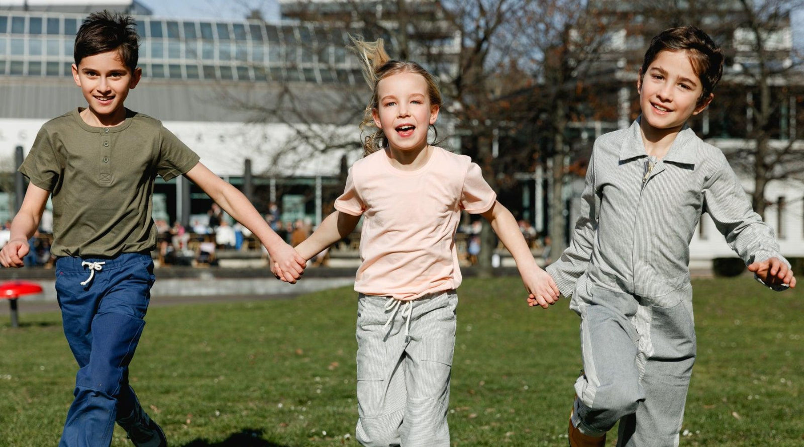 three kids holding hands running through the grass