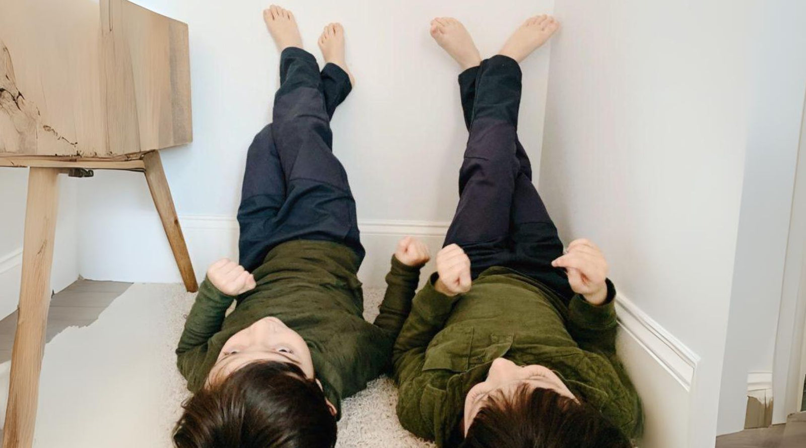 Two boys in Jackalo sustainable kids' clothes lying on carpet, feet up on the wall indoors