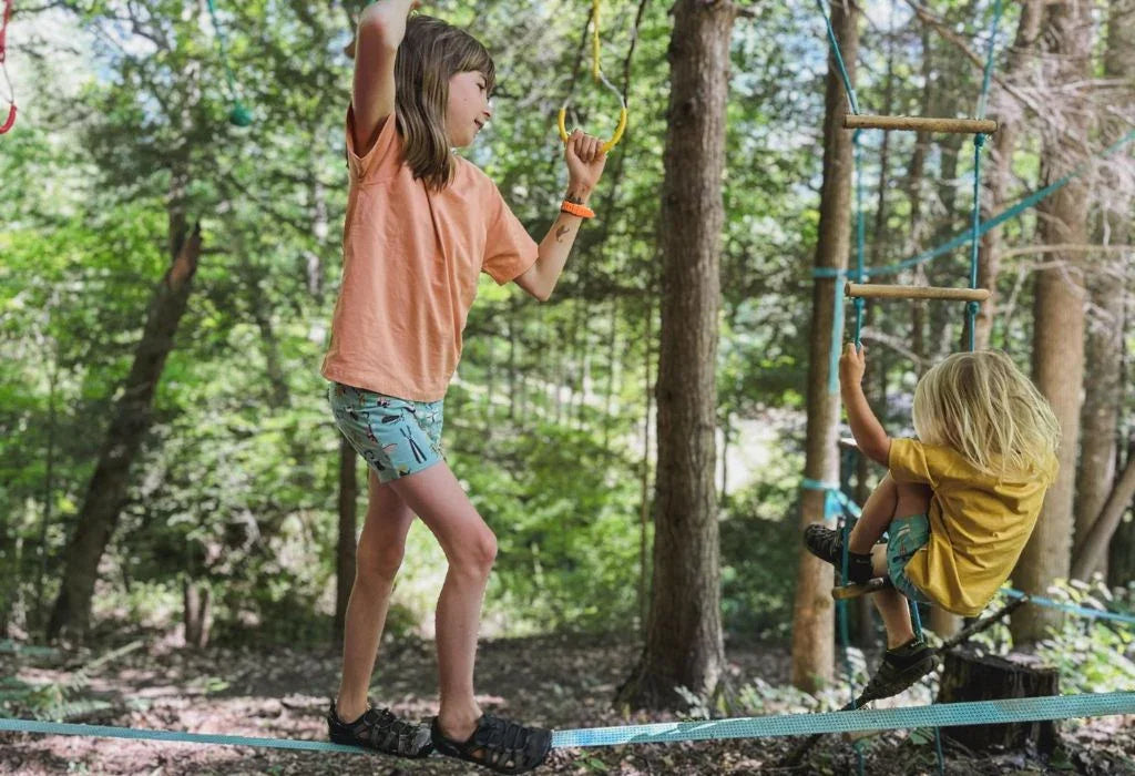 Kids balancing on rope course in forest, wearing active, sustainable clothing for outdoor play