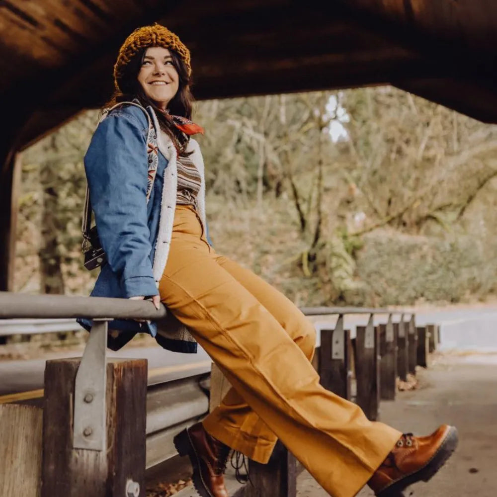 Woman leaning against a railing wearing mustard pants
