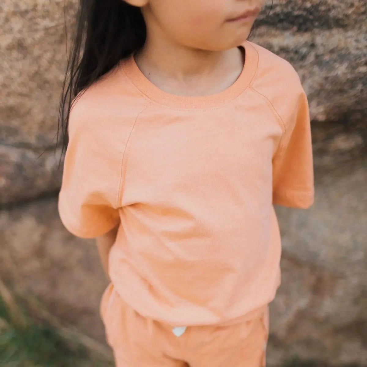 Child in peach Jackalo sustainable kids t-shirt and shorts, outdoors by rocks
