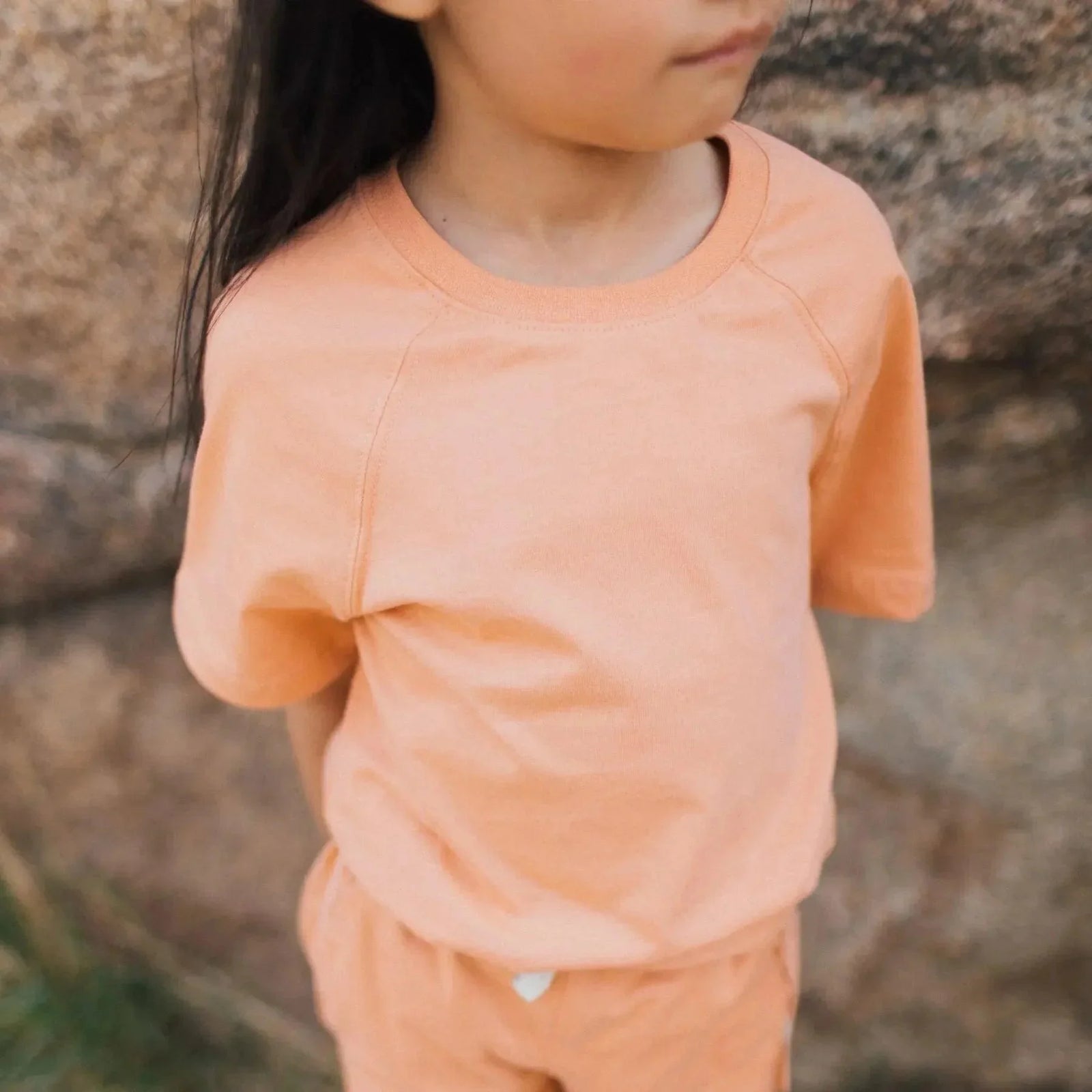 Child in peach Jackalo sustainable kids t-shirt and shorts, outdoors by rocks