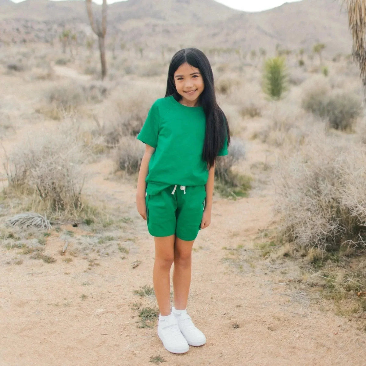 Smiling girl in green sustainable activewear by Jackalo standing outdoors in a desert landscape.