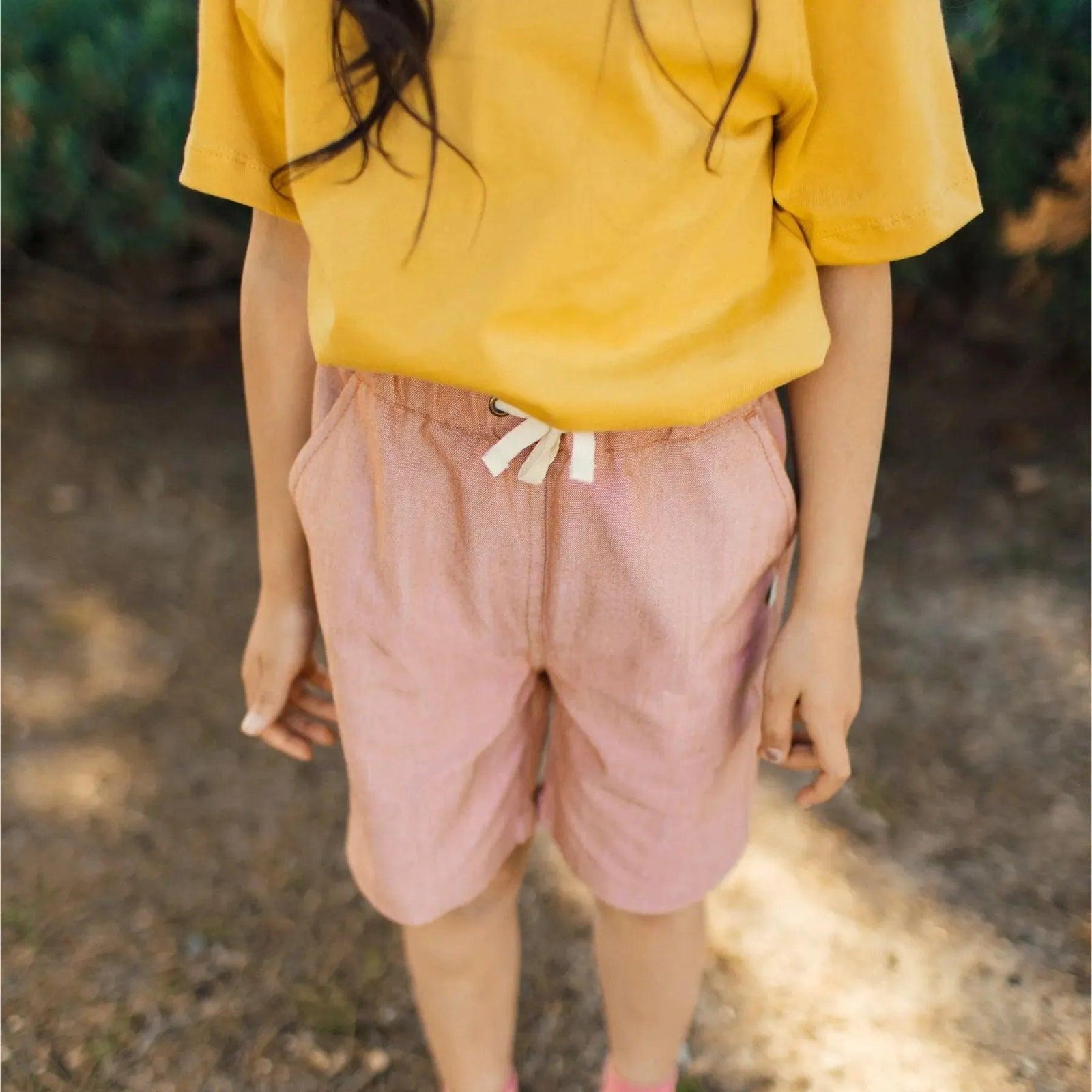 Child wearing a yellow shirt and pink shorts by Jackalo, sustainable kids clothing outdoors.