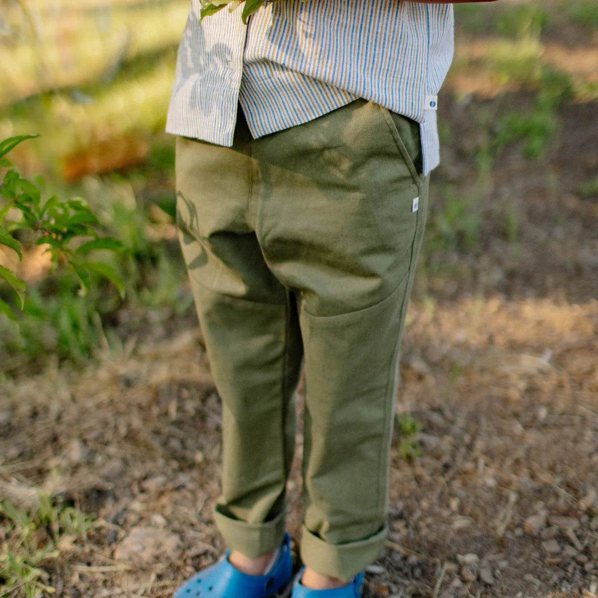 Child wearing olive green sustainable pants by Jackalo outdoors, rolled cuffs, blue shoes