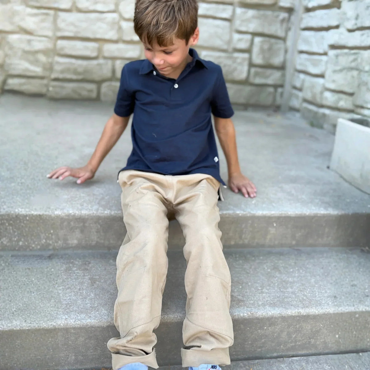 Boy wearing Jackalo khaki Ash Pants sitting on steps, sustainable kids clothing