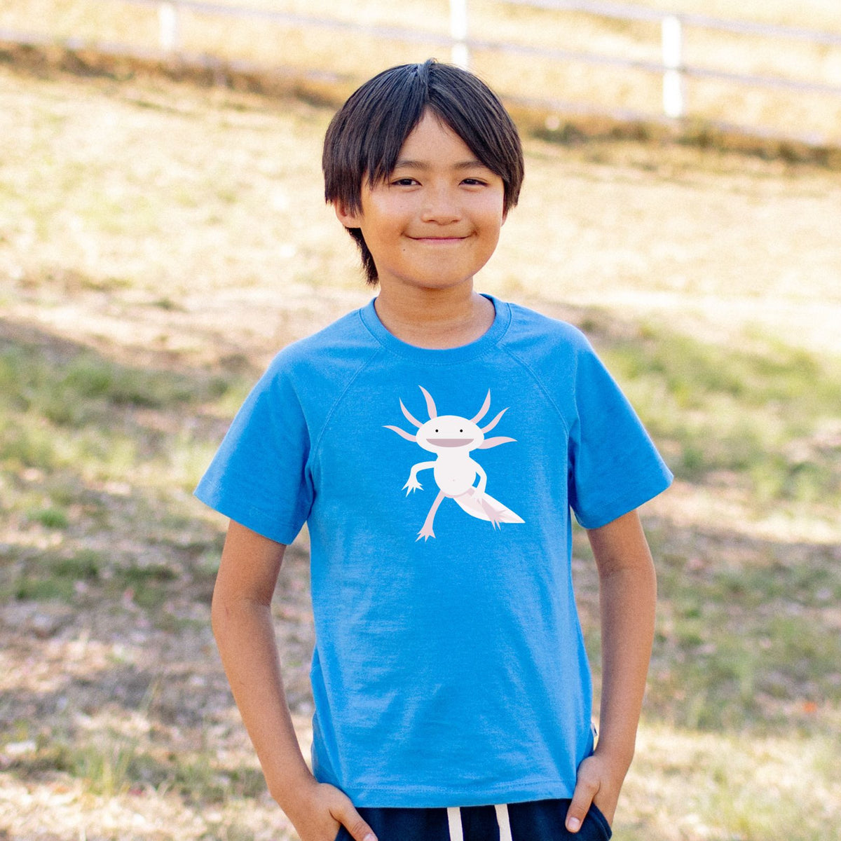 Child wearing a blue t-shirt with a white axolotl graphic outdoors.