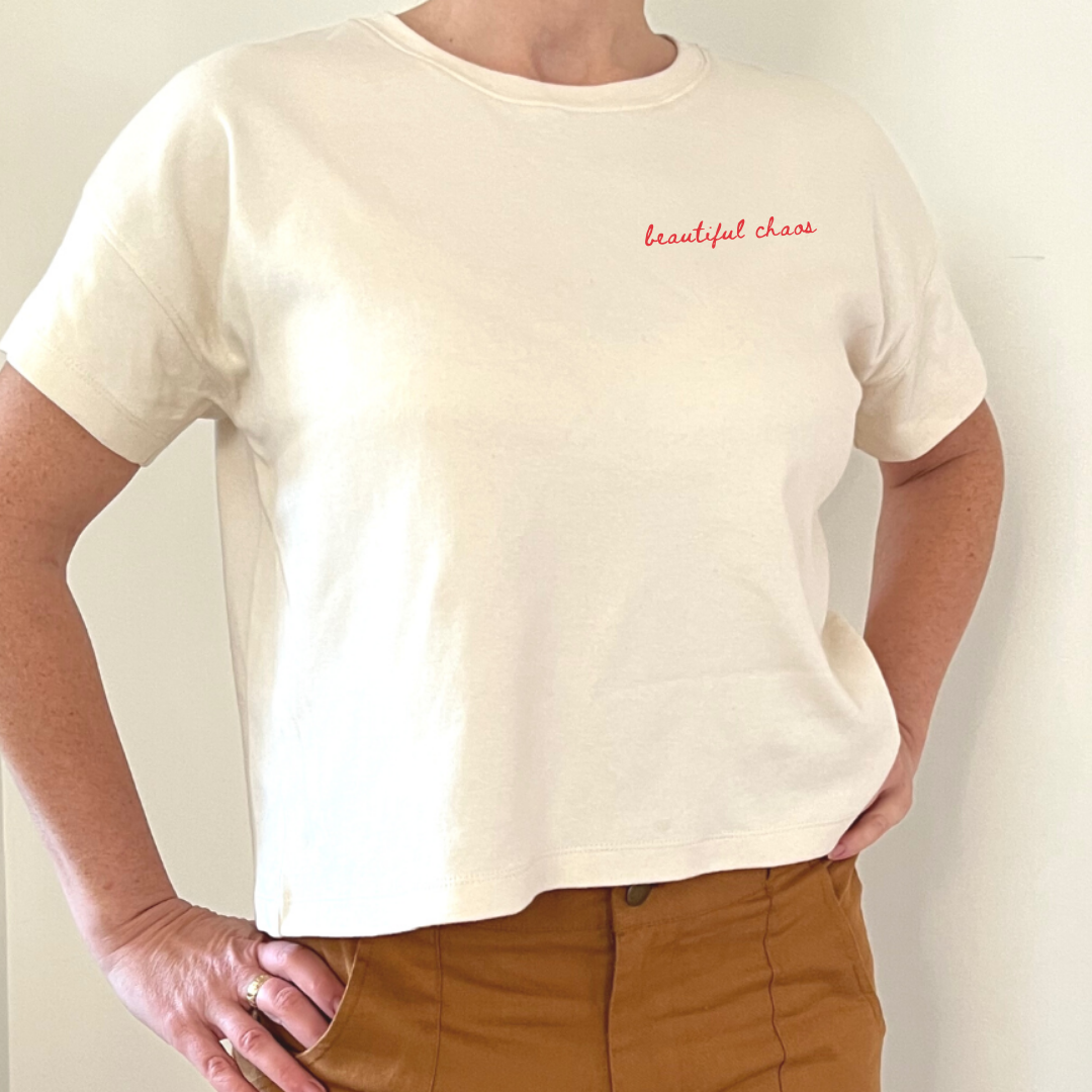 Person wearing a white t-shirt with 'beautiful chaos' text and brown pants against a plain background