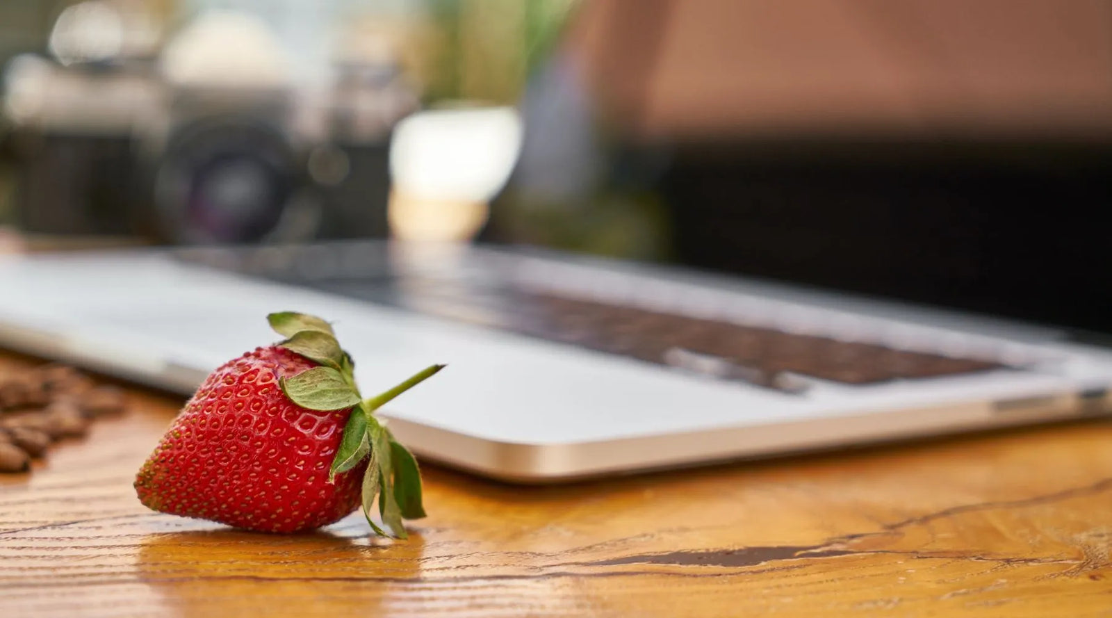 A strawberry beside an open laptop in the table