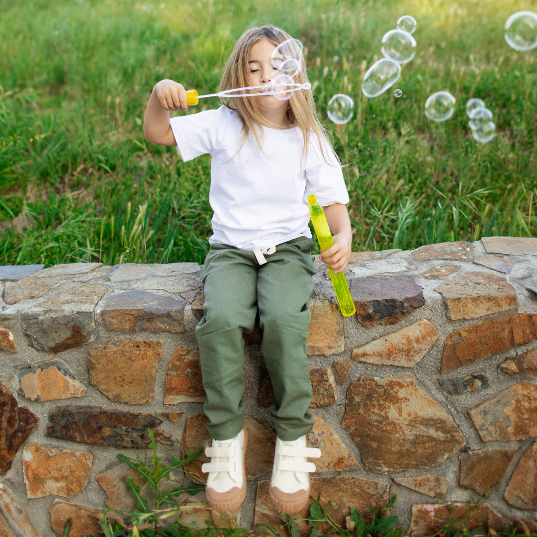 Child blowing bubbles outdoors on a stone wall with grass in the background