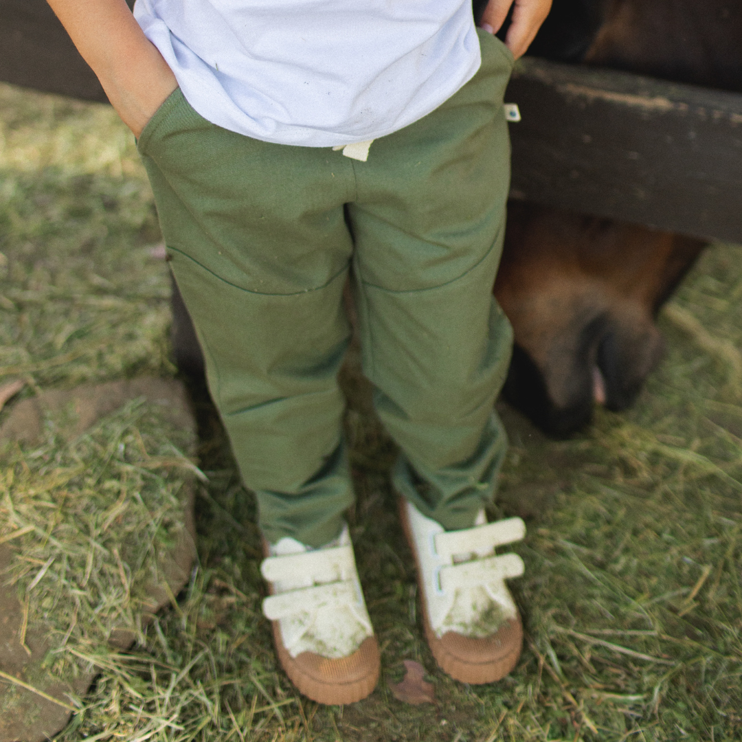 Person wearing green pants and white shoes standing next to a horse on grass.