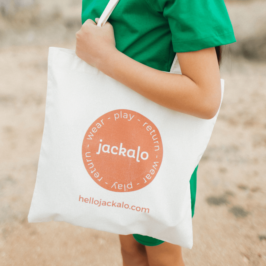 Child holding Jackalo organic tote bag with circular play-wear-return logo outdoors